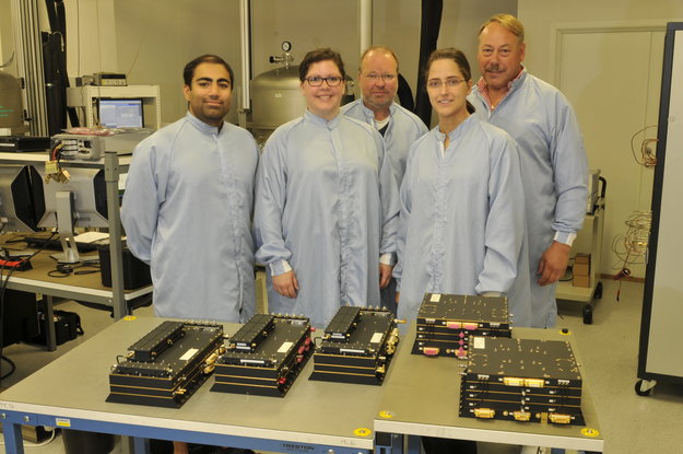 Galileo hardware ready for delivery. The last three Search and Rescue Transponders (SARTs), left, and the last two Frequency Generator and Upconverter Units (FGUUs), right, units produced by Kongsberg Norspace under the first work order for the first 14 Galileo Full Operational Configuration (FOC) satellites being prepared for shipment to Surrey Satellite Technology Ltd, seen together with some of the key project team members.