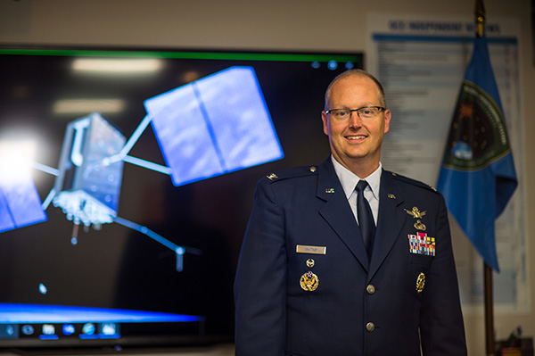 Col. Whitney next to an artist's depiction of a GPS III satellite in orbit. (Photo: U.S. Air Force/Van Ha)