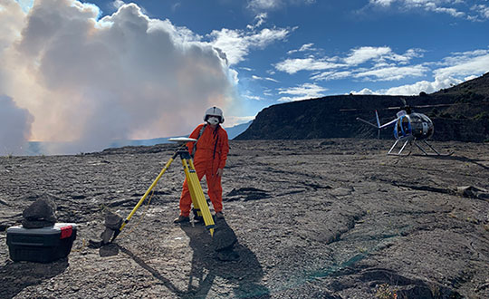 An HVO geophysicist deploys a GPS receiver on the Kilauea caldera floor to measure changes in ground motion. A volcanic gas plume rises in the background. (Photo: USGS)
