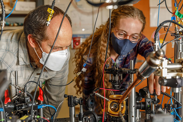 Sandia National Laboratories scientist Peter Schwindt, left, and postdoctoral scientist Bethany Little examine the vacuum package held in a yellow, 3D-printed mount. (Photo: Bret Latter/Sandia) 
