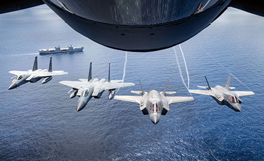 Two U.S. Marine Attack Squadron 211 F-35B Lightning IIs and two U.S. Air Force F-15 Eagles assigned to the 67th Fighter Squadron, fly over United Kingdom aircraft carrier HMS Queen Elizabeth over the west Indo-Pacific region in August 2021. (Photo: USAF/Staff Sgt. Kyle Johnson)