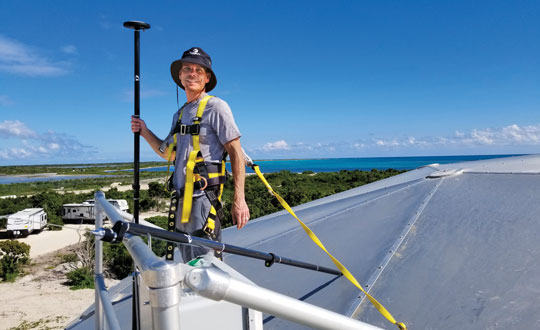 Chris Kahn installing a UHF base station (its antenna is visible in the foreground on a telescopic mast) atop a 50-ft water tower. (Photo: Chris Kahn, AlphaRTK)