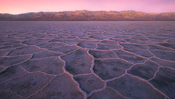 Photo: Landscape of Badwater Basin salt flats, with halite textures under a vibrant pink sky during sunset or sunrise at Death Valley National Park. (Photo: StephenBridger / iStock / Getty Images Plus / Getty Images)